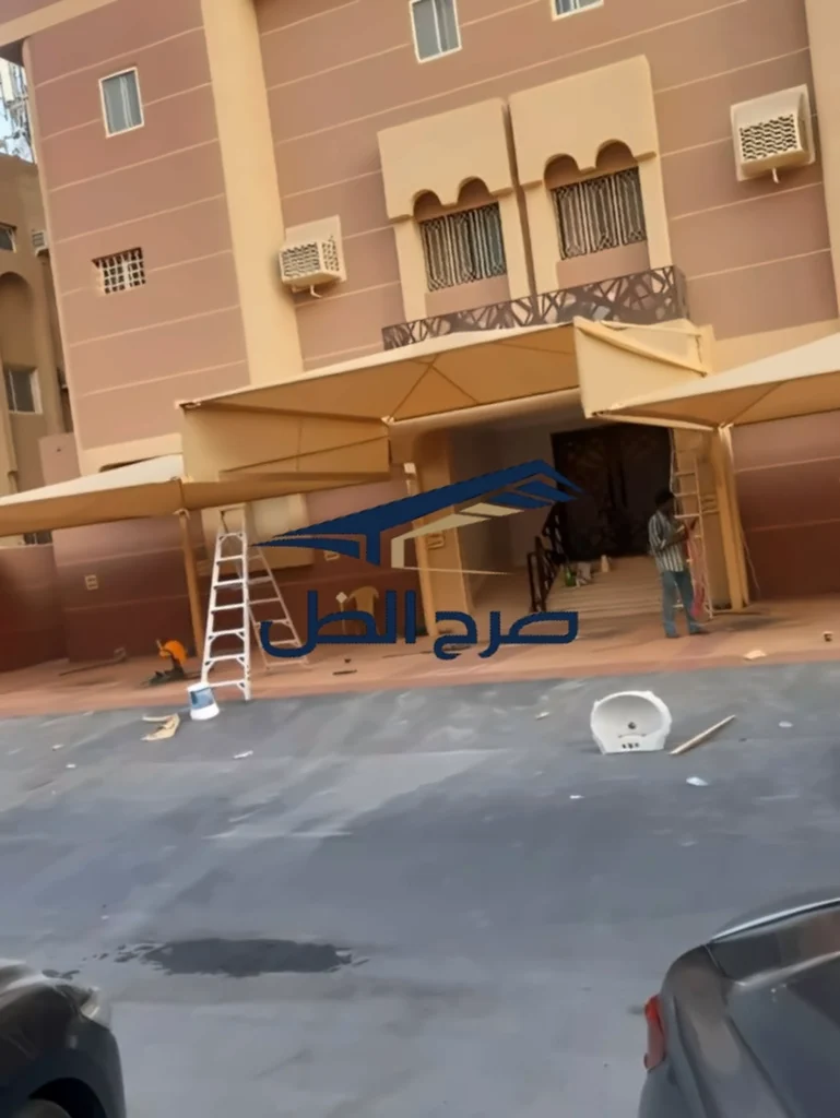 مظلة تغطي مساحة أمام منزل مع سيارة وأثاث خارجي ظاهر.
